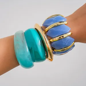 Close-up of stacked acrylic geometric bracelets and chunky blue bangles on arm