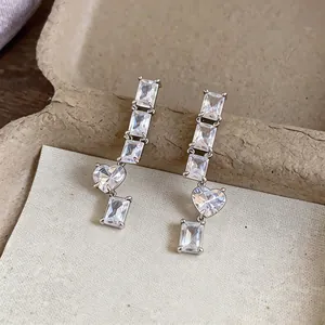 Close-up of elegant silver earrings with sparkling square and heart-shaped zircon stones.