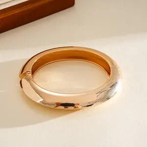 Macro view of chunky gold-toned hinged bangle with smooth mirror polished finish