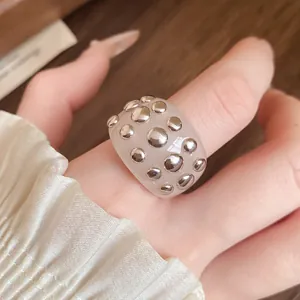 Detailed close-up showing a translucent white resin ring with silver metal studs.