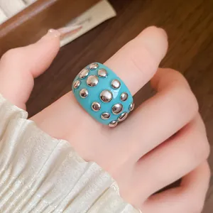 Detailed macro shot of a vibrant turquoise resin ring featuring silver rivets on a hand.