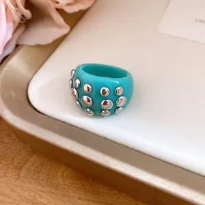 Close-up detail of a turquoise resin dome ring featuring silver round rivet studs decorations