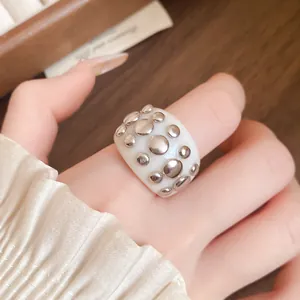 Close-up view of a chic white resin wide ring featuring polished metallic silver studs.