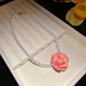 Elegant pearl necklace with large peach rose flower pendant on beige velvet jewelry tray