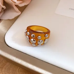 Close-up detail of a chunky amber resin ring decorated with silver metal rivets.