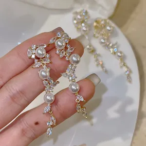 Macro detail of elegant leaf-shaped zircon and white pearl dangle earrings for women