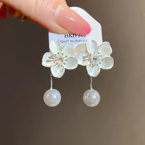 Exquisite detail of white enamel flower earrings featuring silver accents and dangling pearls