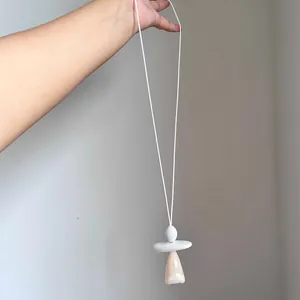 Dettaglio di una collana lunga con pendente geometrico irregolare in pietra color pesca.