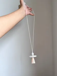 Dettaglio di una collana con ciondolo geometrico minimalista su un lungo cordino bianco.