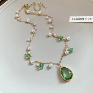 Macro detail of retro gold-tone necklace with emerald green crystals and elegant pearls.