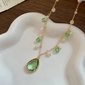 Detailed view of gold necklace with pear-shaped green crystal and pearl accents.