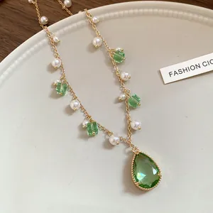 Macro view of a vintage gold necklace featuring a green teardrop crystal and white pearls
