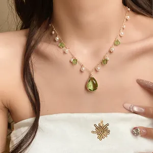 Detailed close-up of a vintage-style green crystal and pearl pendant necklace on a model