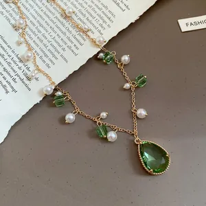 Detail shot of vintage green teardrop crystal and pearl necklace on gold chain.