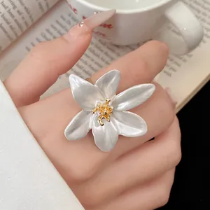 Close-up of vintage white enamel flower ring with textured gold center on finger.