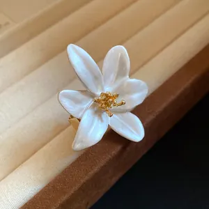 Close-up of elegant white enamel lily flower ring with gold stamen detail.