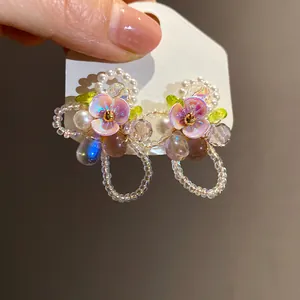 Close-up of handmade flower stud earrings with delicate pearls and cat-eye stones.