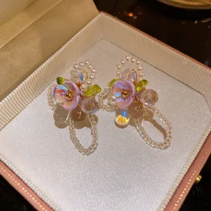 Close-up of floral stud earrings with purple petals, pearls, and cat's eye beads in a box