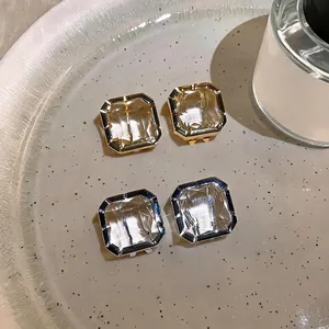 Elegant square faceted glass stud earrings in gold and silver tones on a beige tray