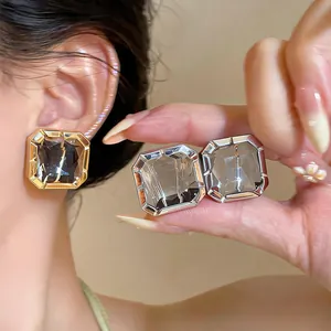 Close-up of elegant square glass stud earrings with faceted grey gems on ear