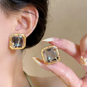 Close-up detail of geometric square stud earrings with gray glass and gold frame on ear