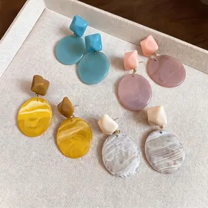 Orecchini a goccia geometrici in resina dai colori vivaci presentati su vassoio beige