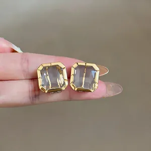 Detailed view of elegant gold-framed square glass stud earrings held against a finger