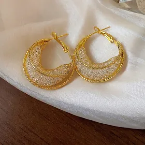 Elegant gold mesh hoop earrings with sparkling glass beads on white silk background.