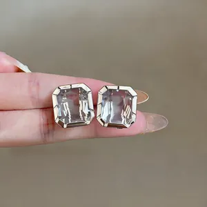 Close-up of elegant square glass stud earrings with silver needle shown on a finger