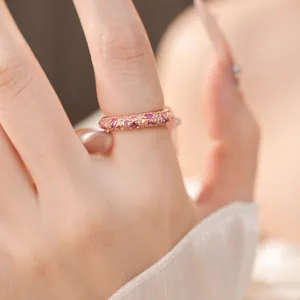 Close-up of a rose gold ring encrusted with pink and white zircons worn on a finger