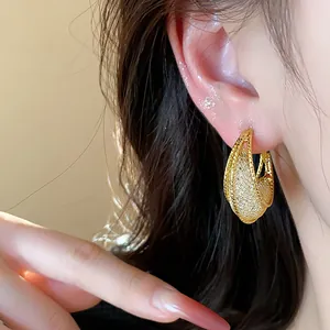 Close-up of elegant gold mesh hoop earrings worn on ear showing textured detail