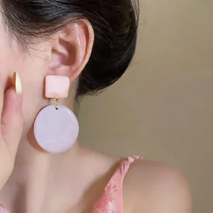 Primo piano di orecchini pendenti geometrici in resina pastello sull'orecchio della modella