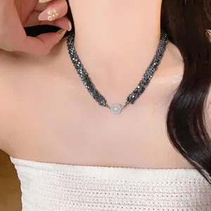Gros plan d'un collier en perles de verre tressées noires avec un pendentif rond scintillant.