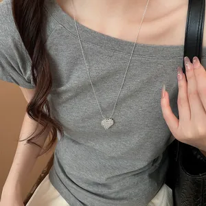 Detailed view of a silver heart pendant necklace worn on a casual grey t-shirt