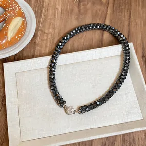 Vue détaillée d'un collier tressé en perles de verre noires avec un fermoir sphérique