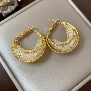 Detailed macro view of elegant gold-toned mesh textured hoop earrings on a grey box.