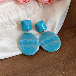 Dettaglio di orecchini in resina marmorizzata blu con pendenti geometrici