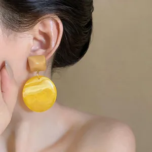 Primo piano di orecchini geometrici in resina con trama marmorizzata gialla indossati all'orecchio