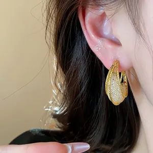 Close-up view of golden glass mesh hoop earrings showing intricate woven texture on ear