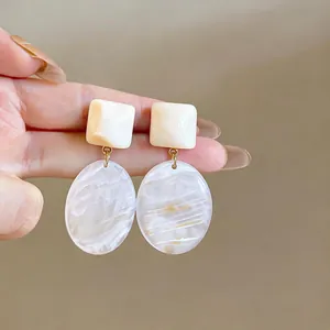 Primo piano di orecchini pendenti geometrici in resina con trame crema e marmo