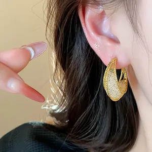 Detailed close-up of golden hollow mesh hoop earrings featuring silver needles