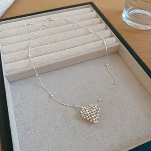 Close-up detail view of a minimalist silver beaded heart pendant on a fine necklace chain.