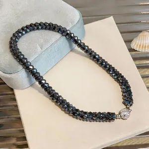 Vue détaillée d'un collier en perles de verre noir tissées avec un fermoir rond brillant.