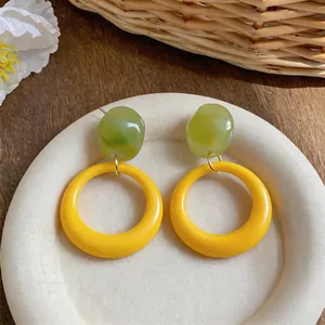 Close-up of vibrant yellow hoop earrings with green resin stone on a textured dish.