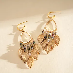 Detailed view of golden water-drop earrings with leaf fringe and colorful beads.