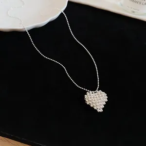 Macro view of a minimalist silver ball chain necklace with a beaded heart pendant.
