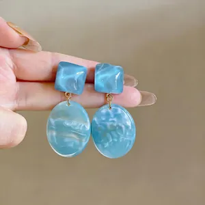 Dettaglio di orecchini a goccia in resina geometrici con vivace trama marmorea blu