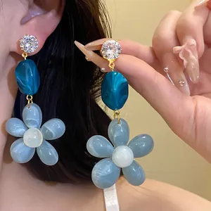 Detailed close-up of blue resin flower drop earrings with sparkling zircon studs.