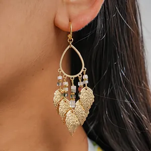 Detail shot of gold-plated teardrop earrings with colorful beads and hanging leaf charms.
