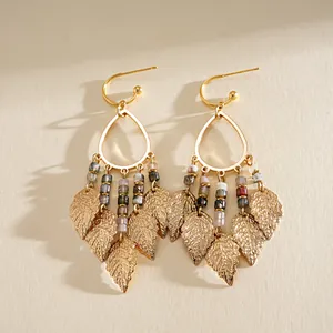 Detail of boho gold leaf drop earrings with colorful stone beads and fringe tassels.